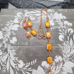 May include: A copper necklace and earrings set with iridescent orange rectangular beads. The necklace is a long, delicate chain with a simple clasp.