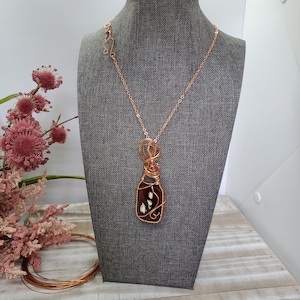 May include: A copper wire wrapped pendant necklace featuring a brown agate stone with white inclusions. The necklace is on a mannequin bust.