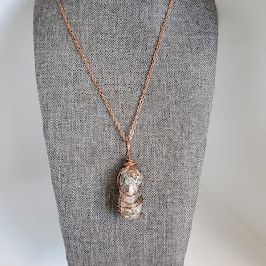 May include: A copper wire wrapped pendant necklace featuring a grey and pink stone with copper chain.