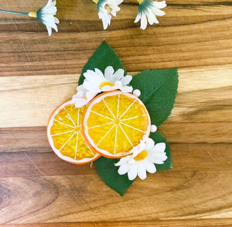 May include: Two orange slices with a white daisy and green leaves on a wooden surface.