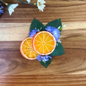 May include: Two orange slices with a decorative arrangement of blue and white flowers and green leaves on a wooden surface.