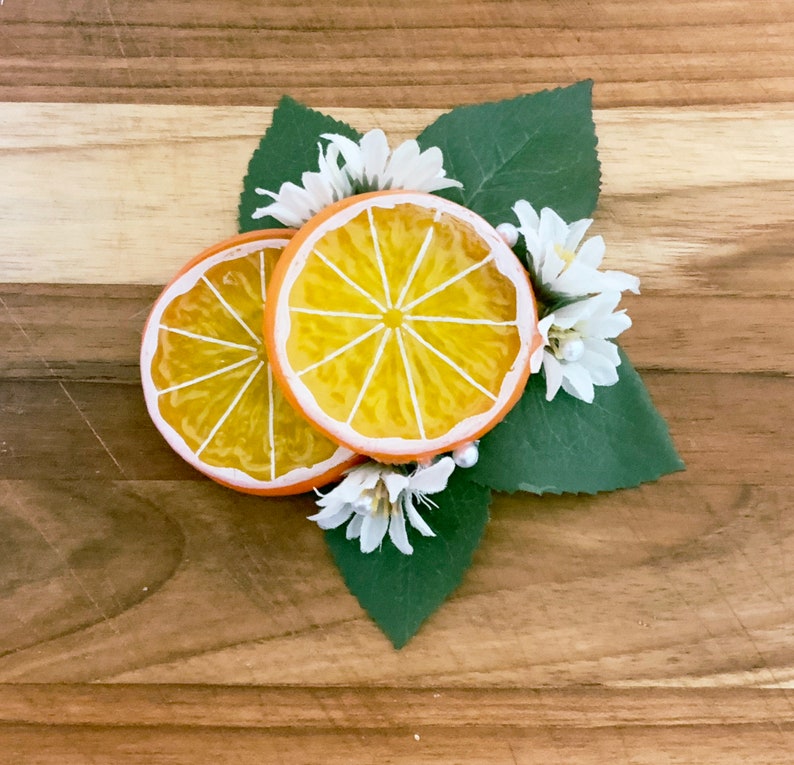 May include: Two orange slices with a white rim, arranged on a bed of green leaves and white flowers.