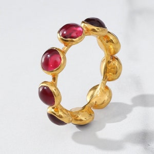 Puede incluir: Anillo de oro con una banda de pequeñas piedras preciosas redondas, rojas y moradas.