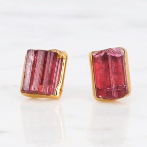 Peut inclure: Une paire de boucles d'oreilles en or avec une pierre précieuse de tourmaline rose brute. La tourmaline est de forme rectangulaire avec une texture striée.