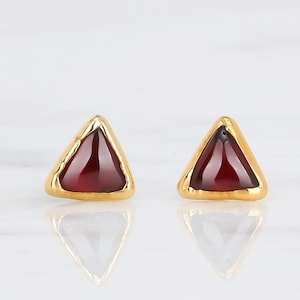 May include: A pair of gold triangle stud earrings with red gemstone accents.