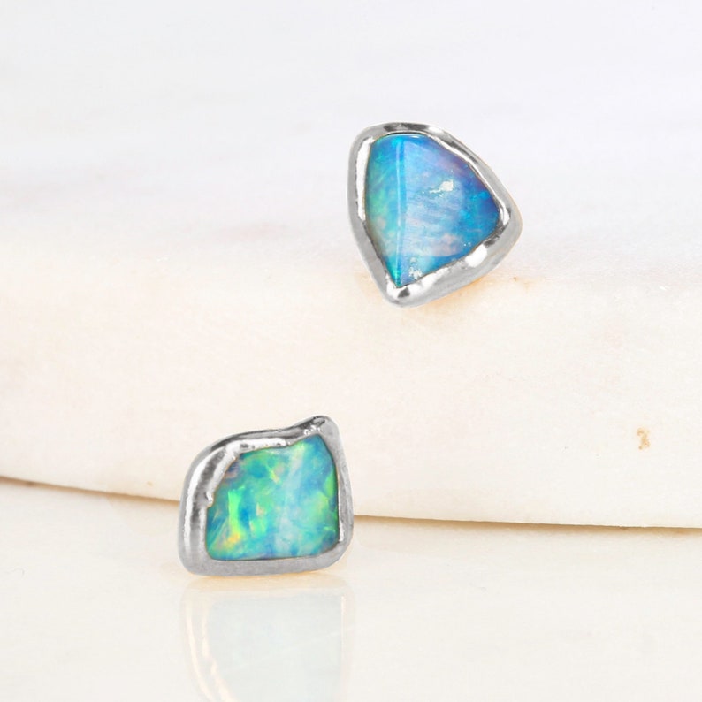 May include: A pair of silver earrings featuring blue opal stones. The stones are set in a rough, irregular shape.