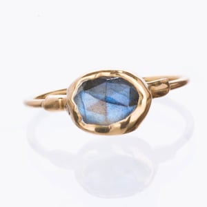 May include: A gold ring with a blue labradorite gemstone. The ring has a simple, organic design.