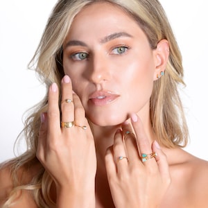 May include: A woman wearing a variety of gold rings with turquoise and opal stones. The rings are on her fingers and are stacked on top of each other.