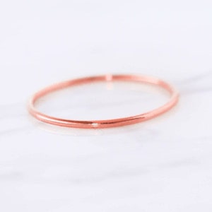 May include: A simple, thin rose gold band ring.
