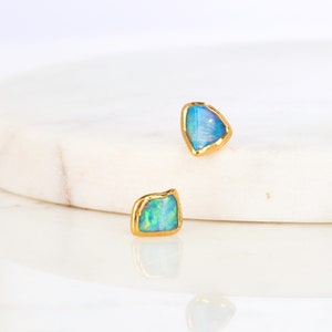 May include: A pair of opal earrings with gold rims, featuring a blue and green iridescent sheen.