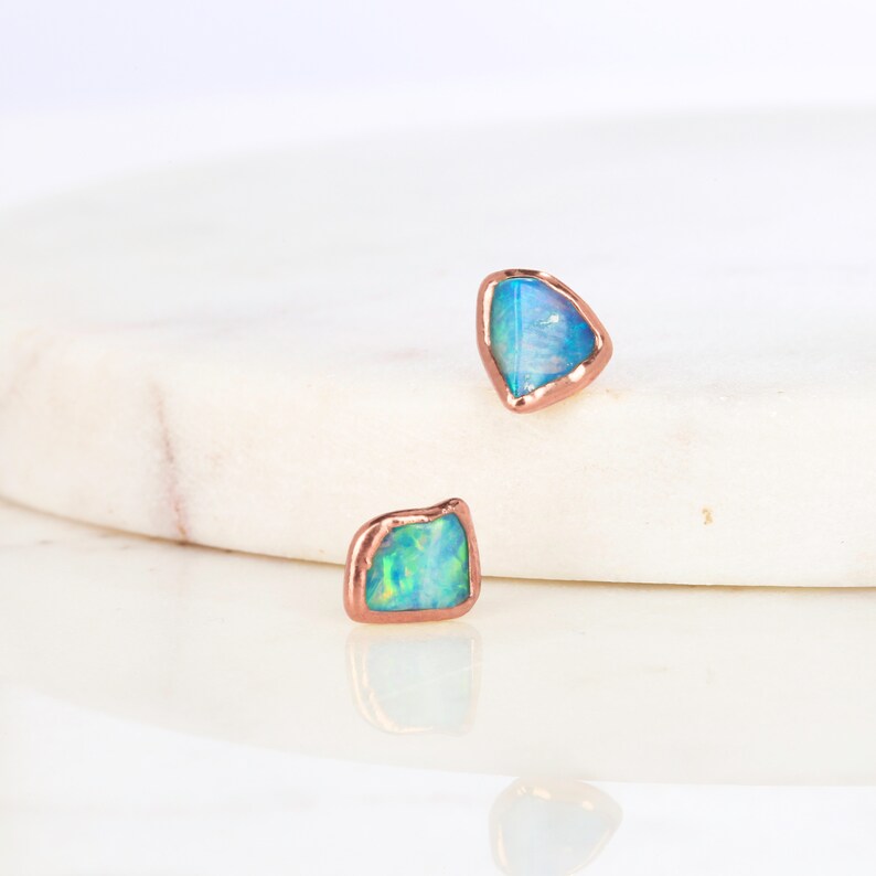 May include: A pair of opal earrings with a rose gold setting. The opals are a light blue colour with a hint of green.