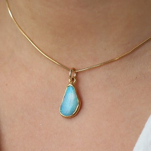 May include: A gold chain necklace with a blue opal pendant. The opal is set in a gold bezel.