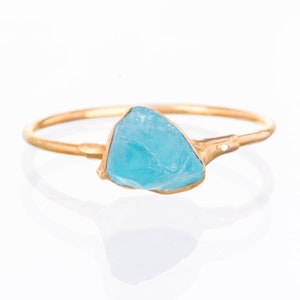 May include: A gold ring with a light blue gemstone. The gemstone is a rough, irregular shape.