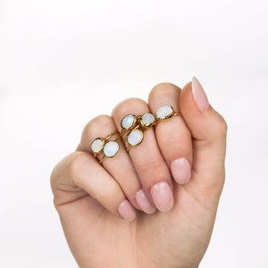 May include: A collection of gold-toned rings featuring small, oval-shaped, iridescent white stones. Each ring has a thin, polished gold band and a bezel setting that secures the smooth, cabochon-style gemstone in place on the finger.
