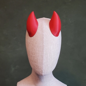 Puede incluir: Una cabeza de maniquí blanca con dos cuernos de diablo rojos unidos a la parte superior.
