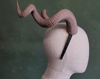 May include: A brown, textured, faux horn headband with a black adjustable strap. The headband is worn on a white mannequin head.