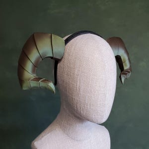 Puede incluir: Una diadema con dos cuernos verdes. Los cuernos están hechos de un material texturizado y tienen un acabado ligeramente iridiscente.