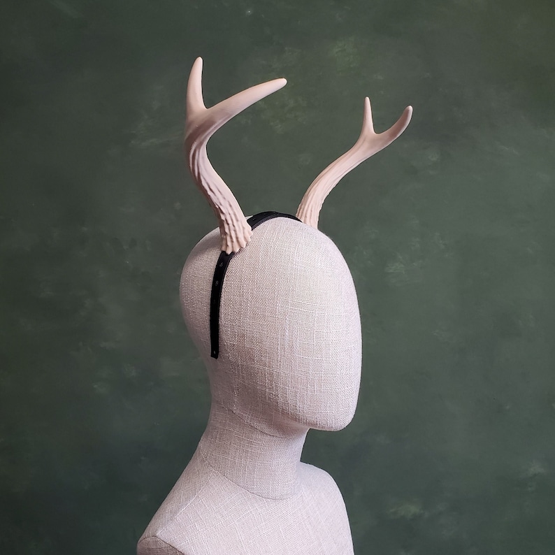 May include: A light pink deer antler headband with a black elastic band. The headband is on a white mannequin head.