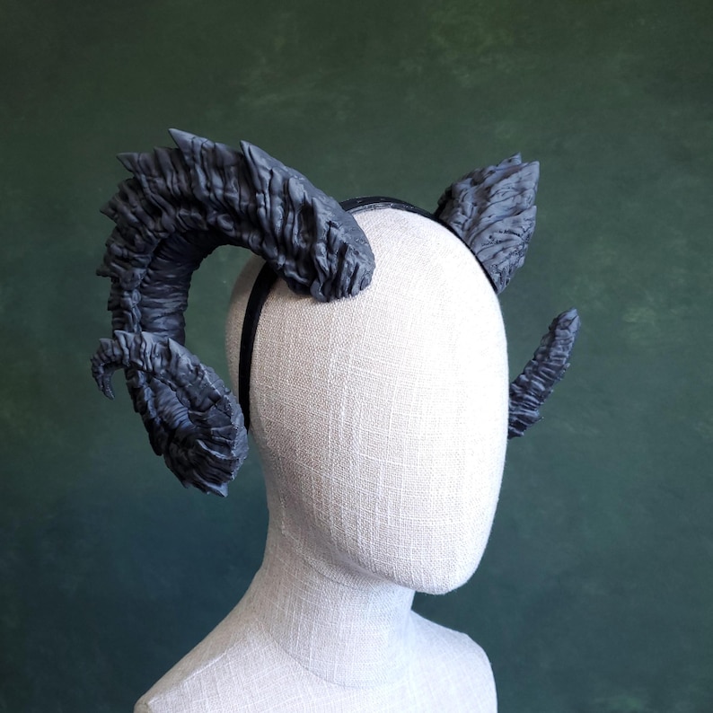 May include: A pair of black, textured, demon horns attached to a black headband. The horns are curved and have a rough, jagged surface.