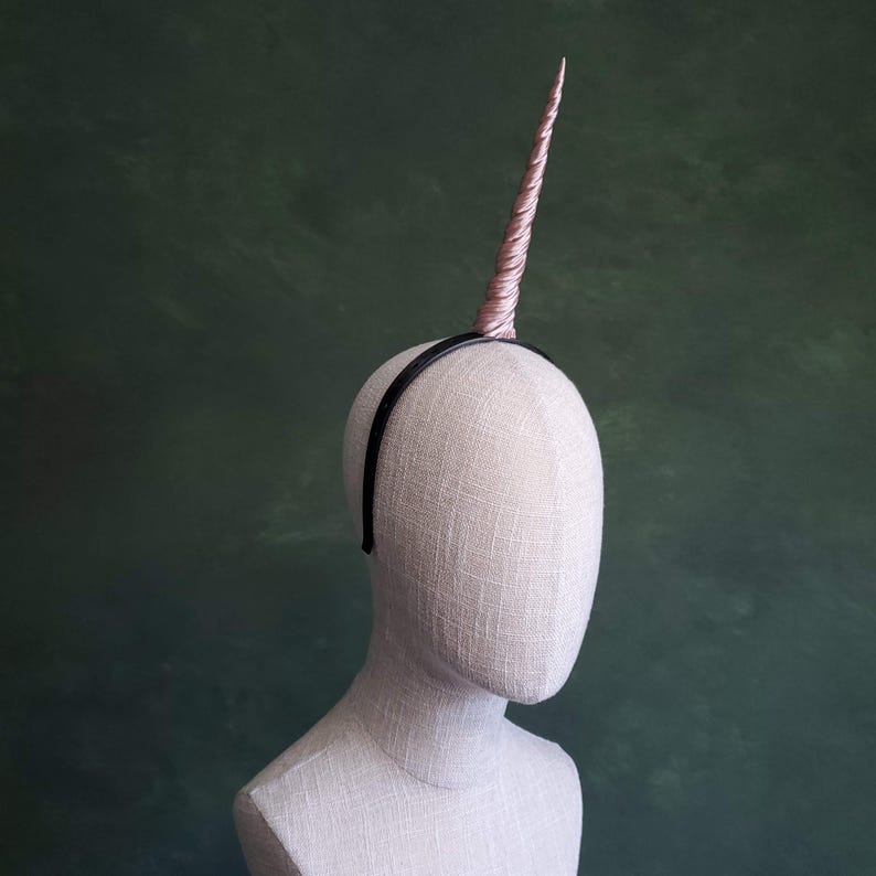 May include: A pink unicorn headband with a black headband. The headband is on a mannequin head.