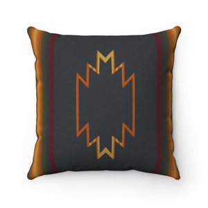 Puede incluir: Una almohada decorativa con un patrón geométrico en tonos naranja, amarillo y marrón sobre un fondo gris oscuro. La almohada tiene una textura tejida y un borde con flecos.