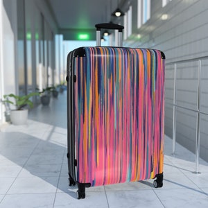 Könnte beinhalten: Ein schwarzer Koffer mit einem farbenfrohen abstrakten Design mit vertikalen Streifen in den Farben Pink, Orange, Blau und Grün.