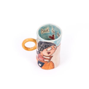 May include: A ceramic mug with a wooden handle. The mug has a cartoon illustration of a girl with a red heart and the text "Back to school" on the side.