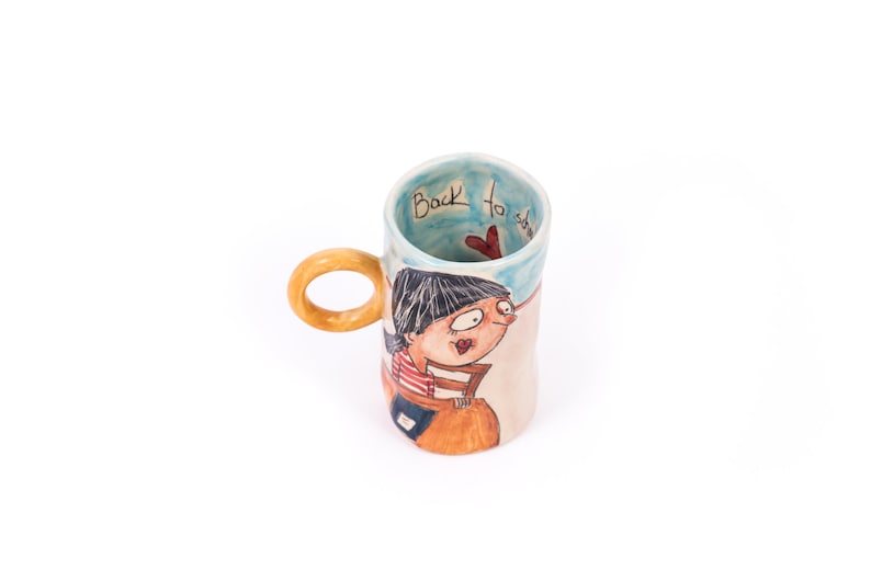 May include: A ceramic mug with a wooden handle. The mug has a cartoon illustration of a girl with a red heart and the text "Back to school" on the side.