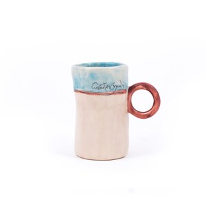 May include: A white ceramic mug with a blue and brown glaze. The mug has a rounded handle and the words "Creative Energy" are written on the side.