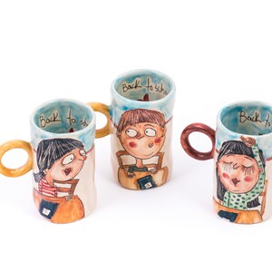May include: Three ceramic mugs with hand-painted illustrations of children and the text "Back to school". The mugs have brown, orange, and red handles.