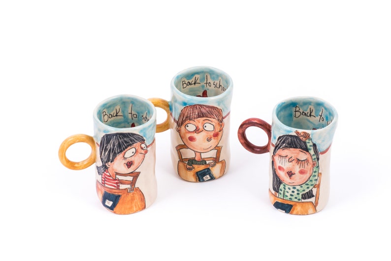 May include: Three ceramic mugs with hand-painted illustrations of children and the text "Back to school". The mugs have brown, orange, and red handles.