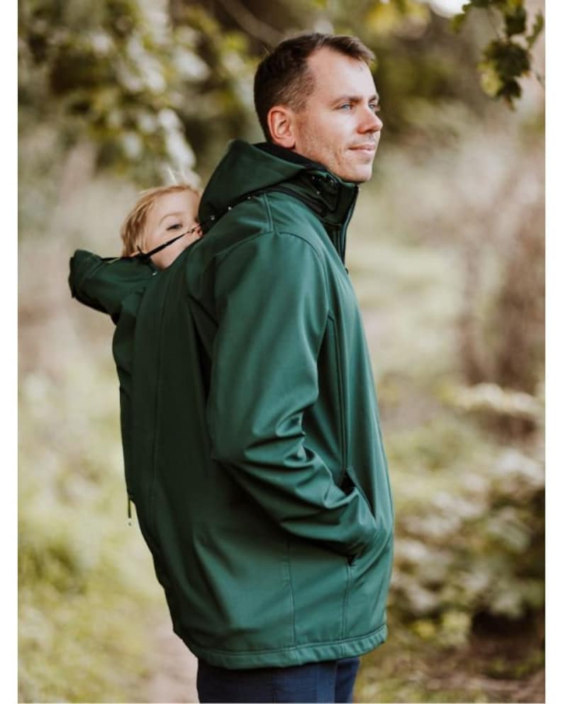 Puede incluir: Una chaqueta verde oscuro con capucha y cierre de cremallera. La chaqueta tiene un bolsillo en el lado izquierdo y un peque&ntilde;o bolsillo en el lado derecho. La chaqueta est&aacute; dise&ntilde;ada para ser usada por una persona que lleva un ni&ntilde;o en la espalda.