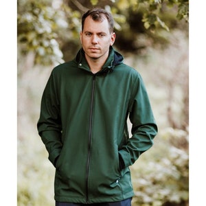 Puede incluir: Una chaqueta softshell verde oscuro con cierre de cremallera y capucha. La chaqueta tiene dos bolsillos con cremallera en la parte delantera.