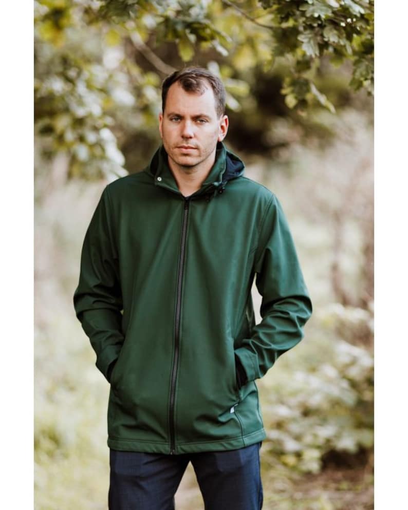 Puede incluir: Una chaqueta softshell verde oscuro con cierre de cremallera y capucha. La chaqueta tiene dos bolsillos con cremallera en la parte delantera.