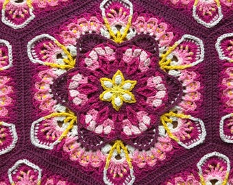 May include: Close-up of a handmade crochet blanket with a floral pattern. The blanket features a repeating design of hexagonal shapes with a central flower motif. The color palette includes shades of purple, pink, yellow, and white, creating a vibrant and textured appearance.