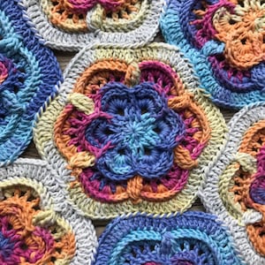 Könnte beinhalten: Nahaufnahme einer gehäkelten Decke aus bunten Quadraten. Die Quadrate sind in Blautönen, Rosa, Orange und Gelb gehalten. Die Decke ist mit einem Granny-Square-Stich gearbeitet.