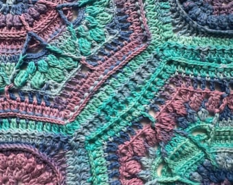 May include: A close-up of a handmade crochet blanket with a patchwork design. The blanket features a variety of geometric shapes in shades of blue, teal, pink, and purple. The texture of the yarn is visible, showcasing the intricate stitch work.
