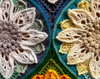 May include: Close-up of a crocheted blanket with a colorful floral pattern. The blanket is made with different shades of blue, green, yellow, and white yarn. The flowers are arranged in a circular pattern, creating a beautiful and intricate design.