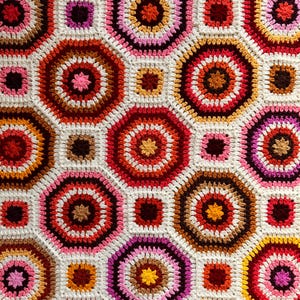 Puede incluir: Una manta de ganchillo con un patrón geométrico de octógonos en tonos de rojo, rosa, blanco, marrón y naranja.