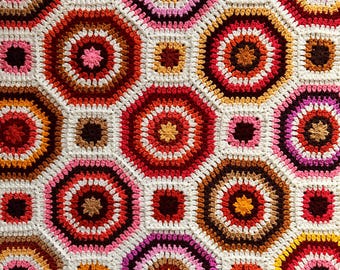May include: A crocheted blanket with a geometric pattern of octagons in shades of red, pink, white, brown, and orange.