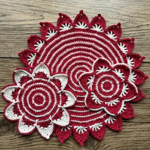 May include: Three crocheted doilies in red and white. The largest doily has a scalloped edge and a circular design. The two smaller doilies are flower-shaped.