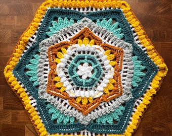May include: A colorful, handmade crochet doily in a hexagonal shape. The design features concentric layers of teal, gray, white, yellow, and orange, creating a floral pattern. The edges are finished with a bright yellow border.