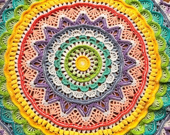 May include: A circular crochet mandala featuring a vibrant spectrum of colors including yellow, lime green, teal, purple, white, and coral. The intricate design consists of concentric rings with varied stitch patterns, including shells and bobbles.