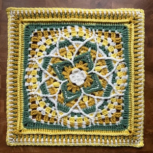 May include: A square, handmade crochet piece featuring a floral design. The piece uses yellow, white, and green yarn. The central flower is white, surrounded by green and yellow petals. The border is yellow with a decorative edge.