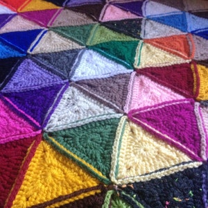 May include: A colorful crocheted blanket made of various shades of yarn, including purple, pink, green, yellow, and white. The blanket is made of triangular patches sewn together to create a geometric pattern.