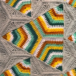 May include: A crochet blanket featuring a geometric pattern of repeating star-shaped motifs. Each motif is composed of concentric layers in shades of gray, white, yellow, dark green, light green, and brown, joined by solid gray yarn.