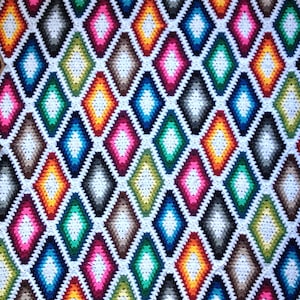 Pode incluir: Um cobertor de crochê colorido com um padrão de diamantes em tons de azul, verde, amarelo, laranja, rosa e branco.