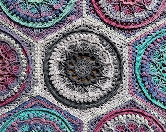 May include: A hexagonal crochet blanket with a repeating pattern of colorful mandala designs. The blanket is made with a variety of shades of purple, pink, teal, and gray yarn.