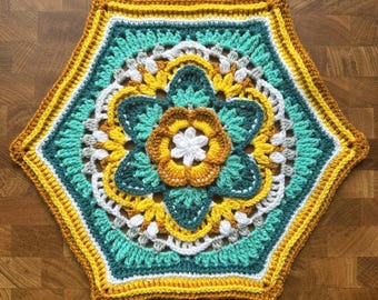 May include: A handmade, hexagonal crochet doily featuring a floral design. The doily showcases a vibrant color palette of teal, yellow, white, and brown. The central flower is surrounded by intricate crochet patterns, creating a decorative and textured piece.