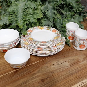 Può includere: Un set di piatti in ceramica bianca con un motivo floreale con accenti arancioni, gialli e verdi. Il set comprende ciotole, piatti e tazze.